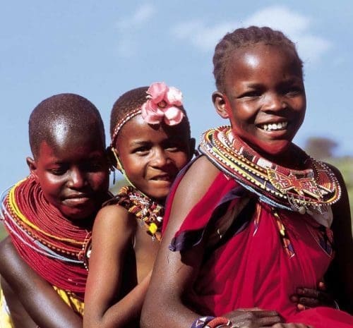 A group of joyful Maasai children with beaming smiles, wearing vibrant traditional clothing, enjoying a Tanzania safari adventure amidst the stunning natural beauty of the grasslands