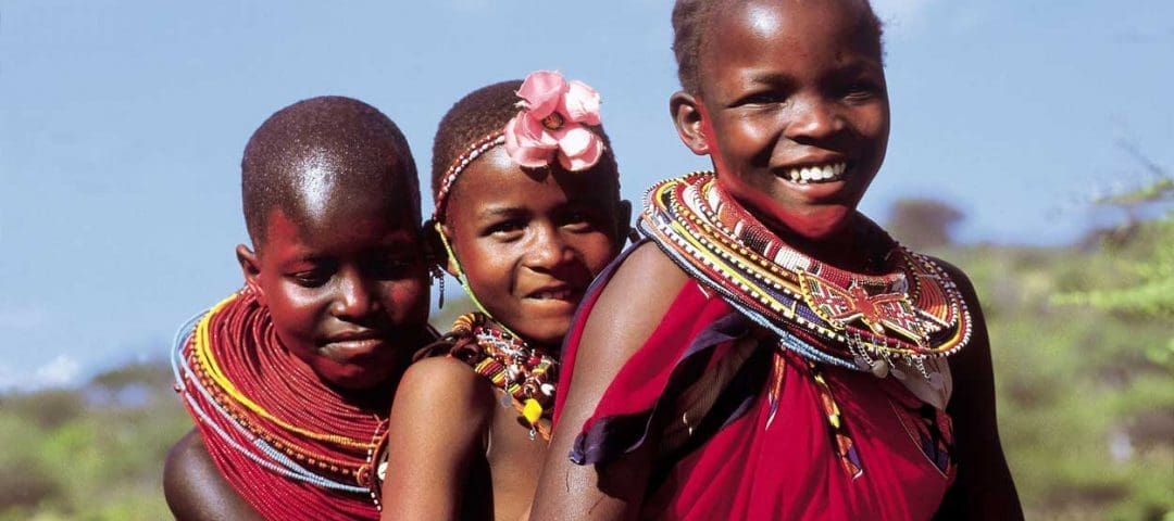 A group of joyful Maasai children with beaming smiles, wearing vibrant traditional clothing, enjoying a Tanzania safari adventure amidst the stunning natural beauty of the grasslands